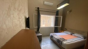 Een slaapkamer met een bed, een bureau, een stoel, een raam met gordijnen en een plafondventilator.