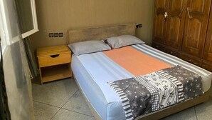 Een slaapkamer met een bed, een houten nachtkastje, een kledingkast en een betegelde vloer.