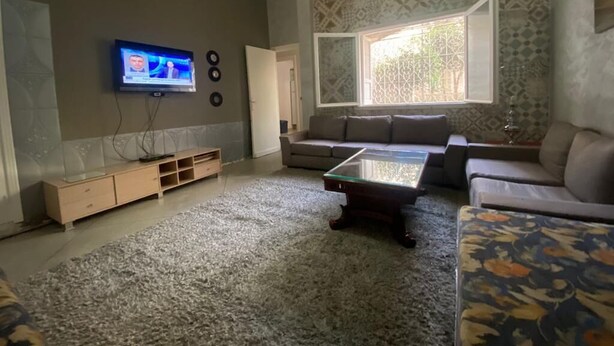 Een woonkamer met een bank, een salontafel, een televisie en een behang met patroon.