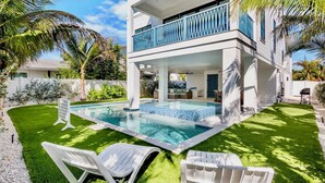 Uma casa de dois andares com piscina, espreguiçadeiras brancas e uma varanda.