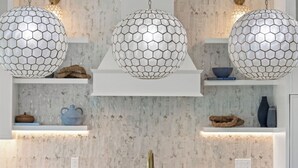 Cozinha com ilha central, luminárias pendentes e painel de fundo branco.