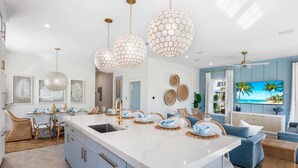 Cozinha moderna com uma ilha grande, luminárias pendentes e um espaço de refeições com mobiliário de vime.