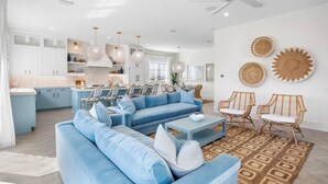 Uma sala de estar moderna com um sofá azul, uma mesa de centro, cadeiras de vime e um tapete estampado.