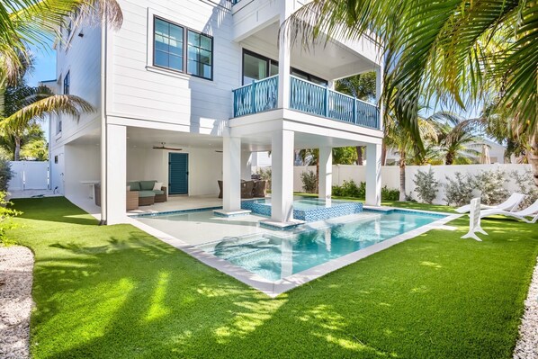 A modern two-story house with a swimming pool, outdoor seating, and palm trees.