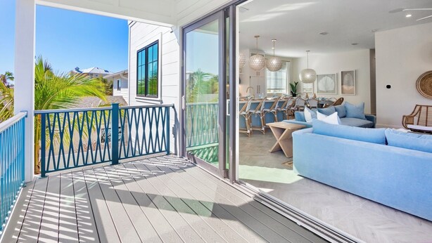 Uma sala de estar moderna com uma grande porta de vidro deslizante que dá para uma varanda, um sofá azul e uma área de jantar com mesa e cadeiras.