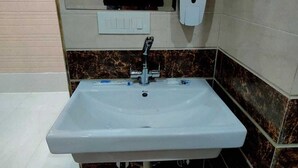 A bathroom with a white sink, a faucet, and a soap dispenser on the wall. - AS Hotel Expoinn (Greater Noida)