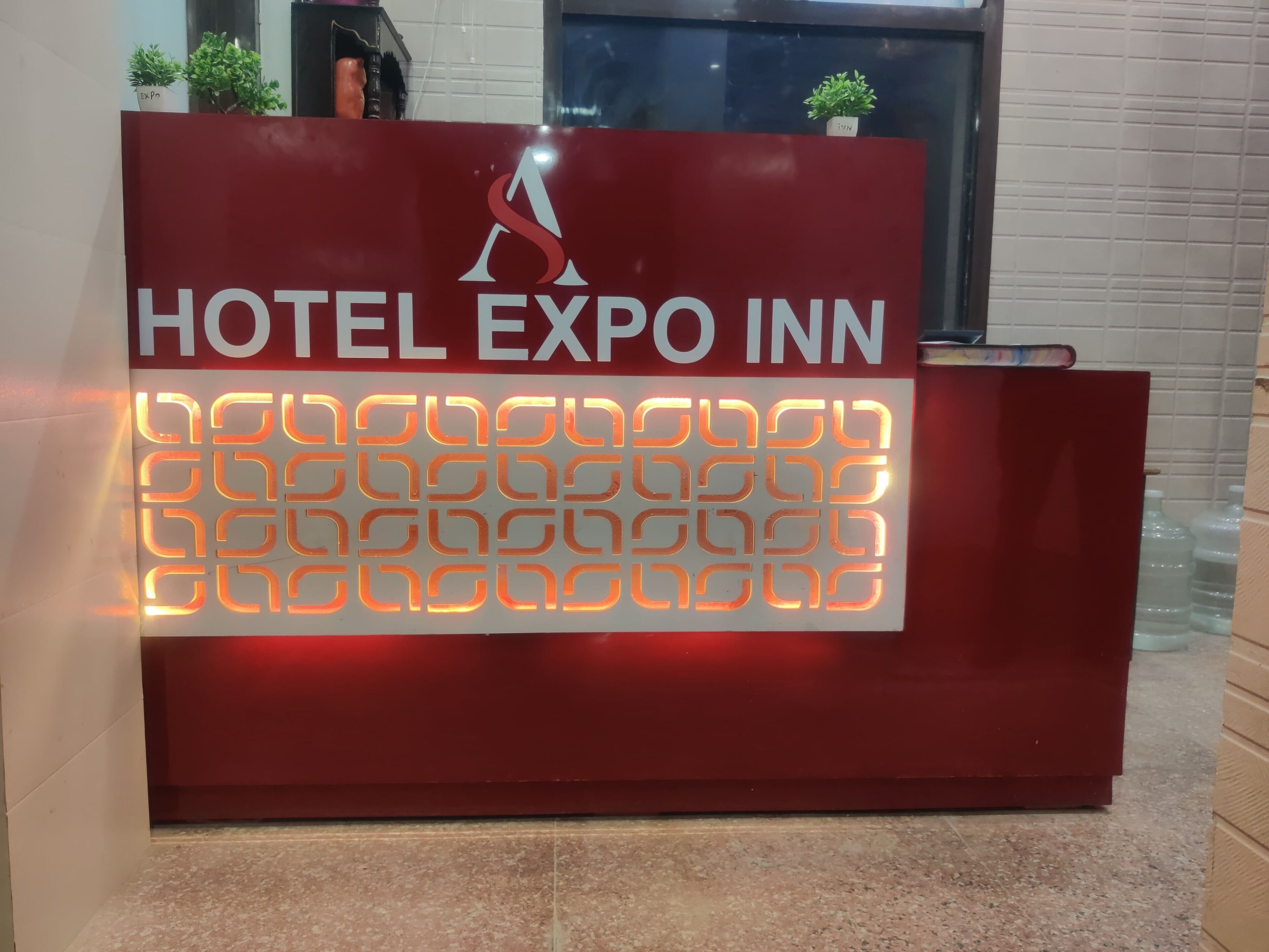 Un comptoir d’accueil rouge sur lequel on peut lire le texte « HOTEL EXPO INN » et au-dessus duquel figure un logo.
