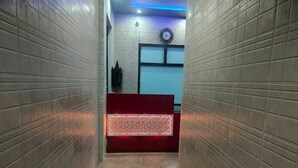 A narrow hallway with tiled walls, a red reception desk, and a clock on the wall. - AS Hotel Expoinn (Greater Noida)
