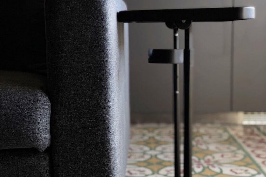 Un coin de pièce avec un canapé noir à la texture particulière et un présentoir en métal noir.