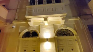 Fachada de edificio con dos puertas simétricas, cada una con un pequeño ventanal encima y un accesorio de iluminación en el centro.