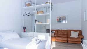 Ein modernes Schlafzimmer mit einem Bett, weißen Nachttischen, einem braunen Ledersofa und einem weißen Bücherregal.
