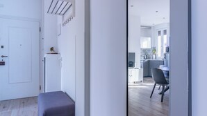 Ein modernes Interieur mit Holzboden, einer Bank, einer weißen Tür und Blick in einen Küchenbereich mit Esstisch und Stühlen.