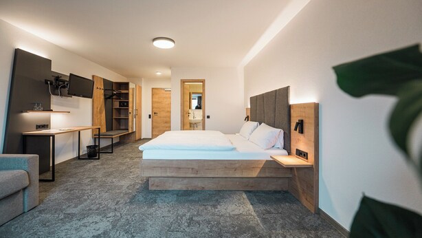 A modern hotel room with a large bed, a desk with a computer, a TV mounted on the wall, and a wardrobe. - Hotel Goldener Engel (Ihringen)
