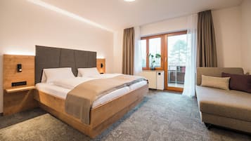 Habitación de hotel con una cama de madera, un sofá, una ventana con cortinas y vistas al exterior.
