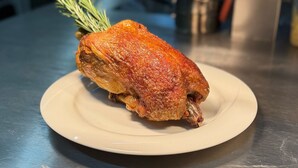 A roasted chicken on a white plate on a stainless steel counter. - Hotel Goldener Engel (Ihringen)