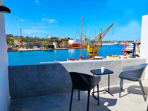 A balcony with two chairs and a table, overlooking a harbor with cranes and a cruise ship. - Cabin 4 Savynomad Harbour Residences Seaport Views (Cospicua)