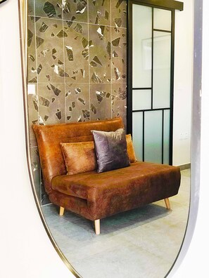 A modern sofa with wooden legs and a cushion, positioned against a wall with a geometric tile pattern.