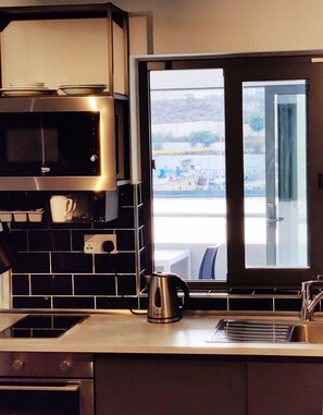 Une cuisine équipée d’un four à micro-ondes, d’une bouilloire et offrant une vue sur un pont et l’eau, grâce à une porte vitrée.