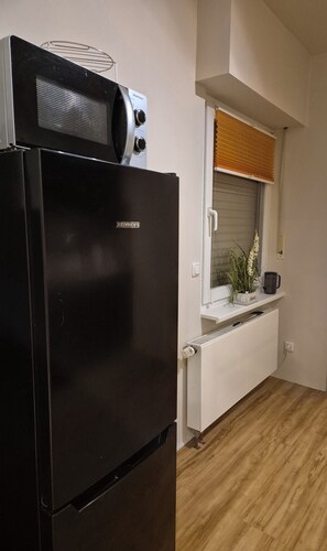 Kitchen area with a refrigerator, oven, and window with a blind.