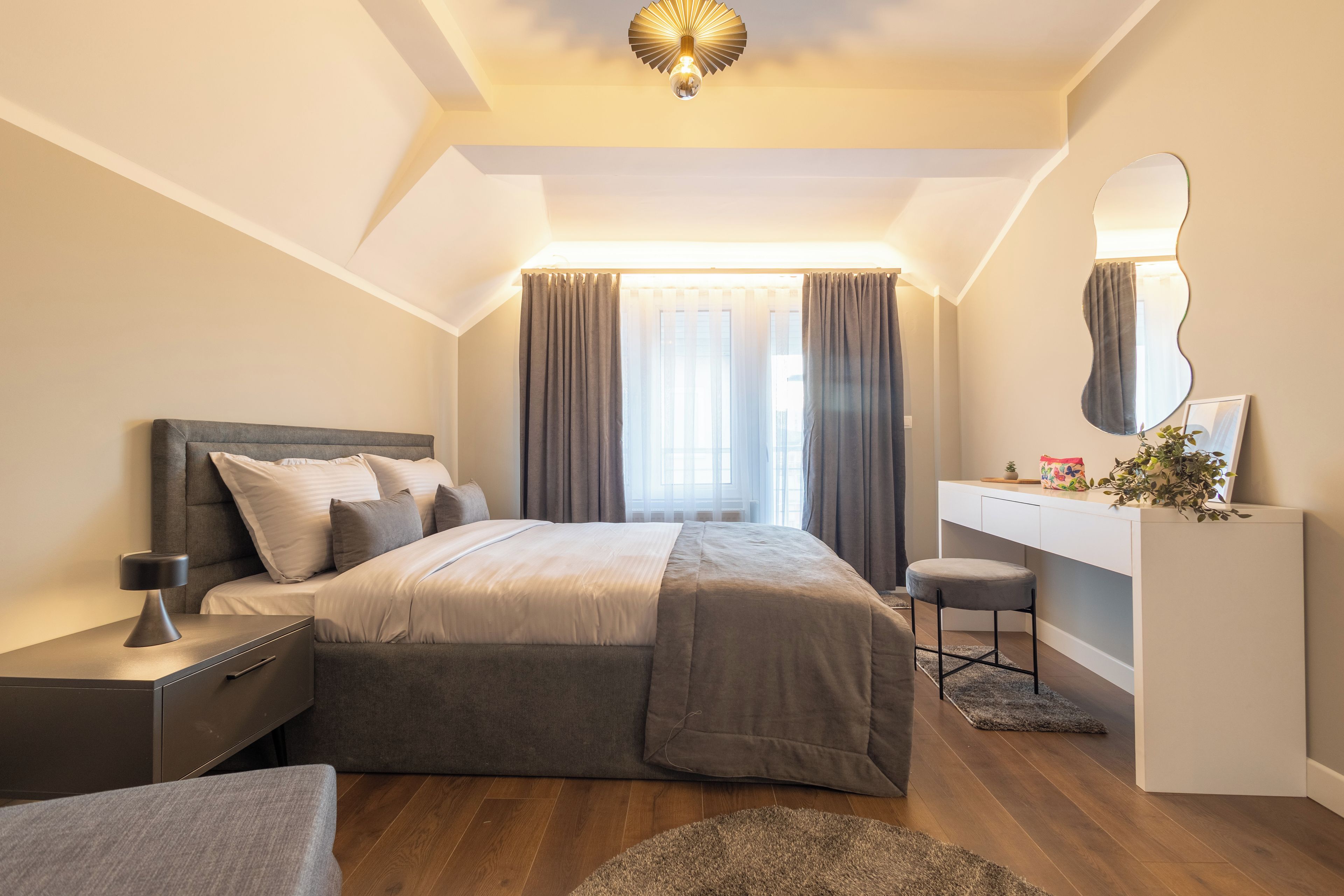 Une chambre moderne avec un lit, des tables de chevet, un bureau, un miroir et une fenêtre avec des rideaux.