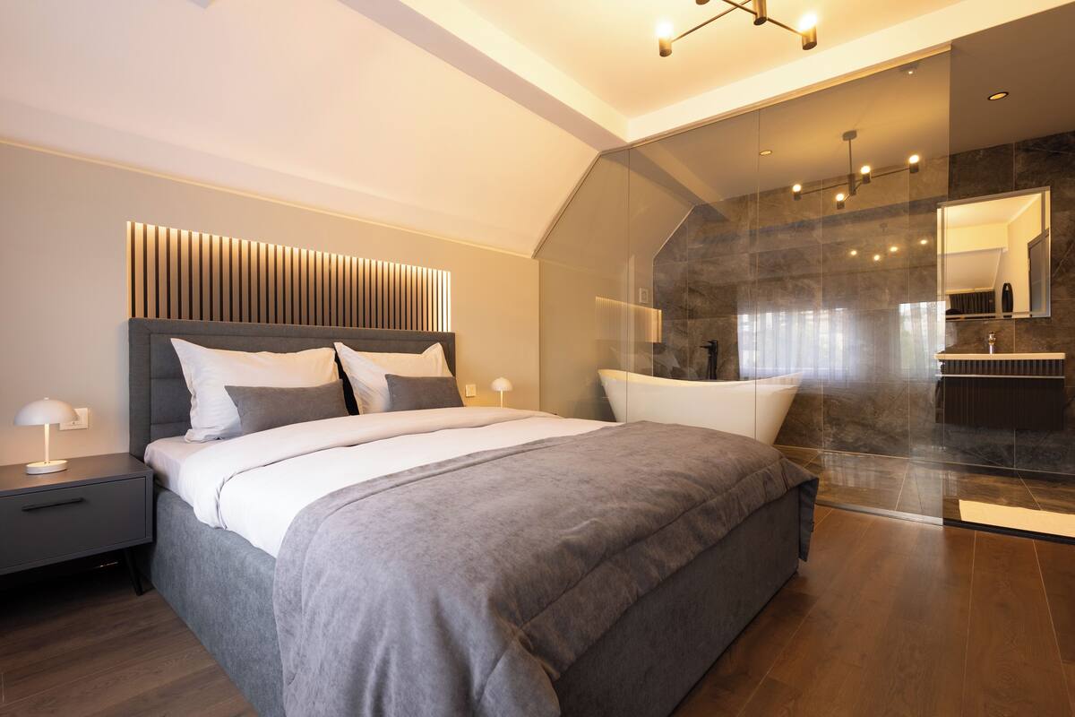 A modern bedroom with a large bed, a bedside table with a lamp, and a glass shower area.