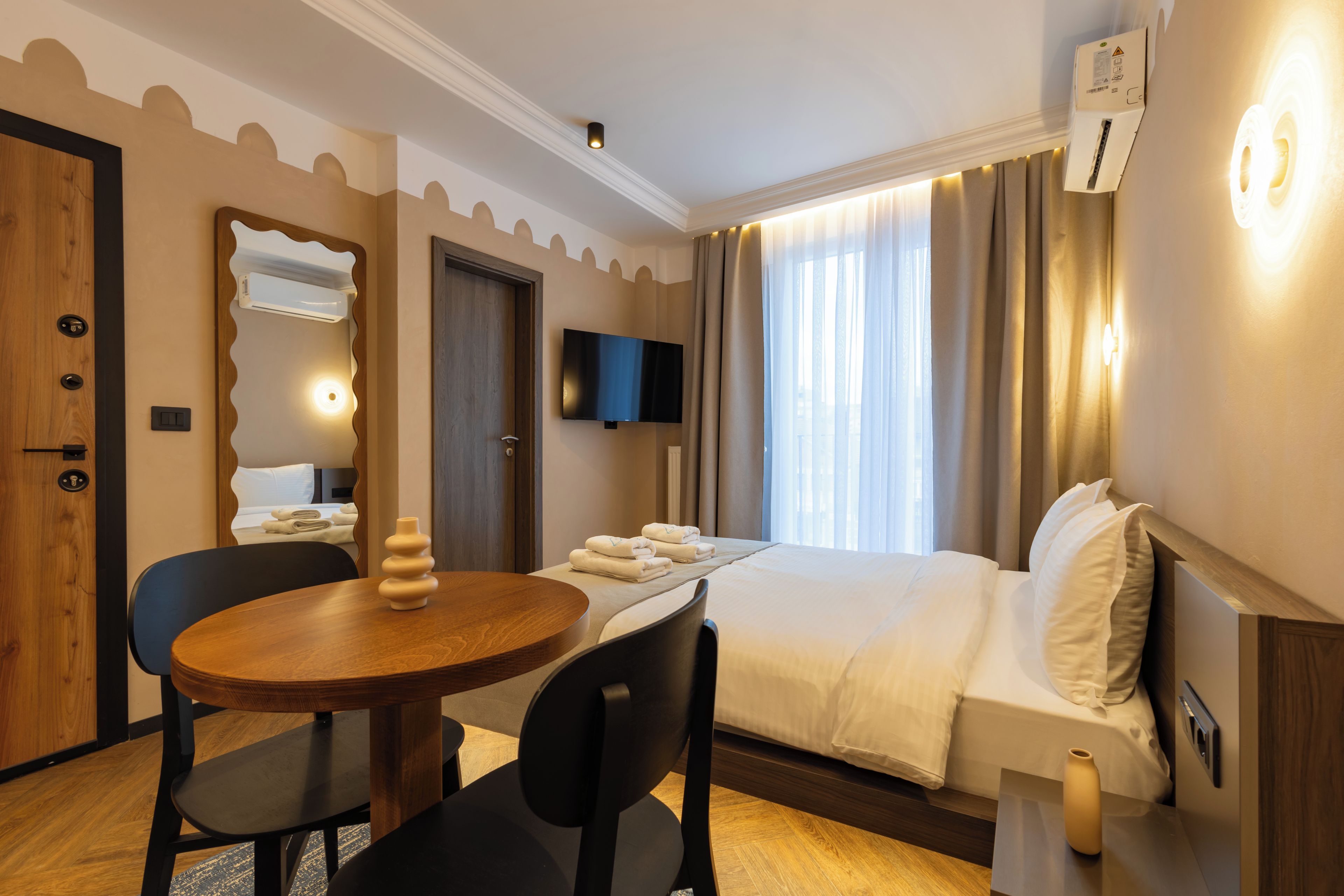 Habitación de hotel con cama, escritorio, silla, televisor y espejo.