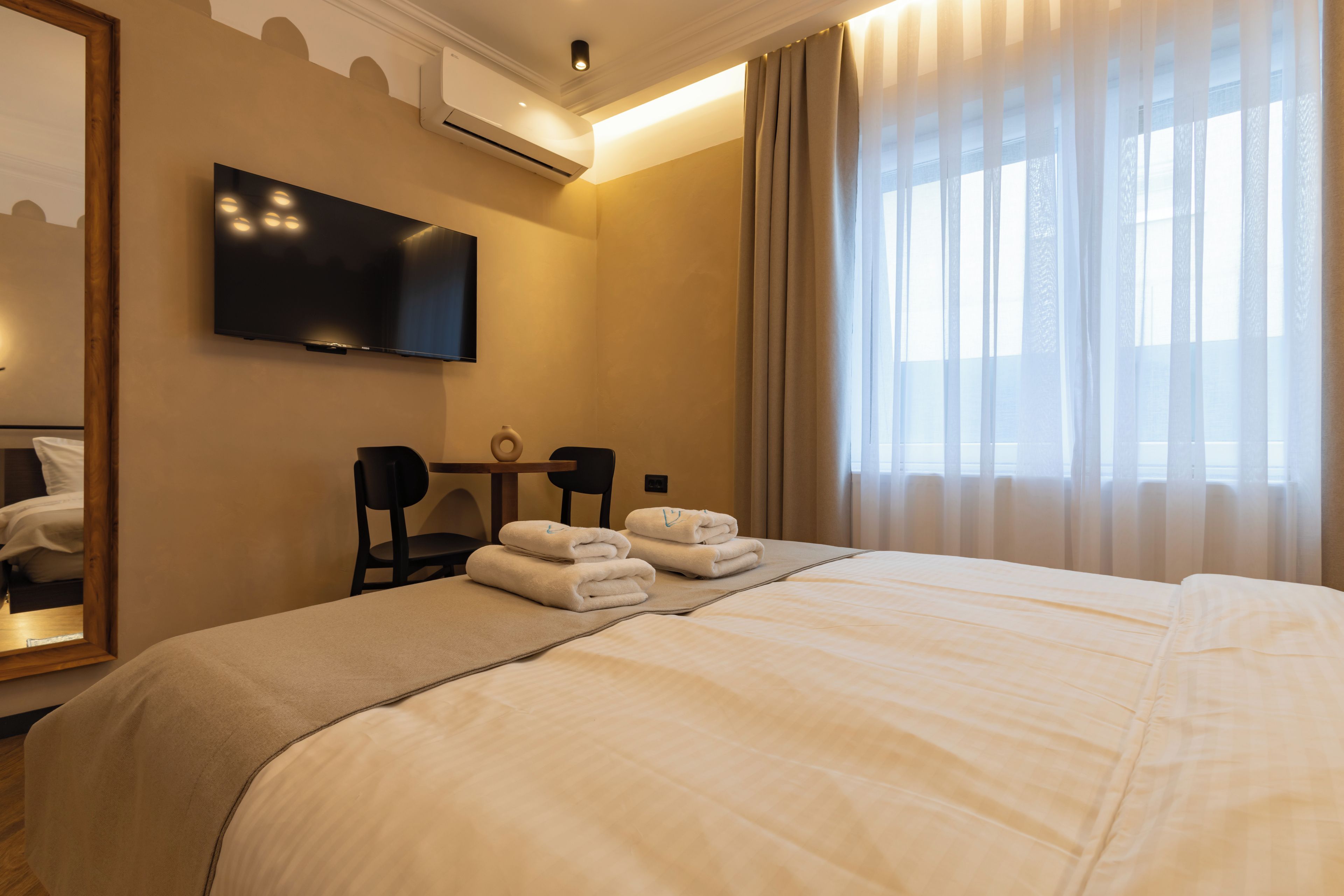 A hotel room with a bed, a television, a desk with chairs, and a window with curtains.