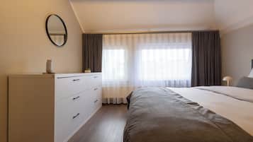 Een slaapkamer met een bed, een dressoir, een spiegel en een raam met gordijnen.