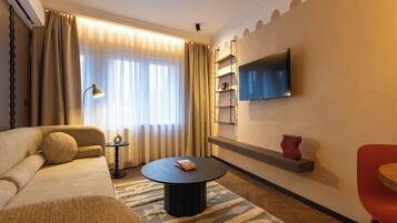 Un salon moderne avec un canapé, une table basse, un téléviseur fixé au mur et un fauteuil rouge.