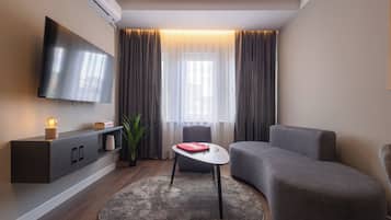 Een moderne woonkamer met een flatscreen-tv, een grijze bank, een klein rond tafeltje en een potplant.