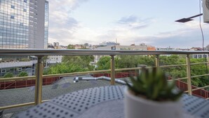 Un balcón con planta en maceta, barandilla de metal y vista panorámica de la ciudad.