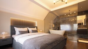 A modern bedroom with a large bed, a bedside table with a lamp, and a glass shower area. - Prishtina City Apartments (Pristina)