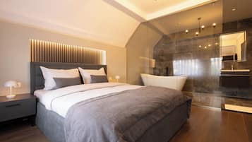 Un dormitorio moderno con una cama grande, una mesita de noche con lámpara y una zona de ducha con mampara de cristal.
