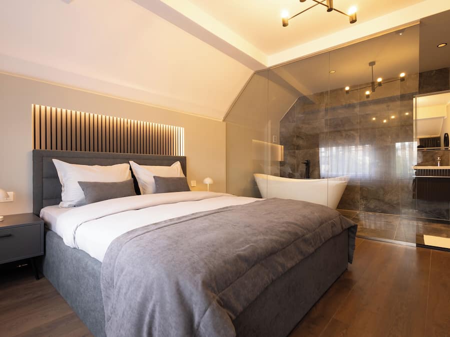 A modern bedroom with a large bed, a bedside table with a lamp, and a glass shower area.