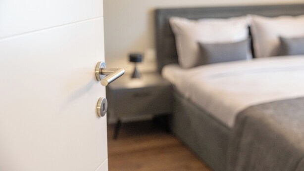 A bedroom with a bed, a nightstand, and a door. - Prishtina City Apartments (Pristina)