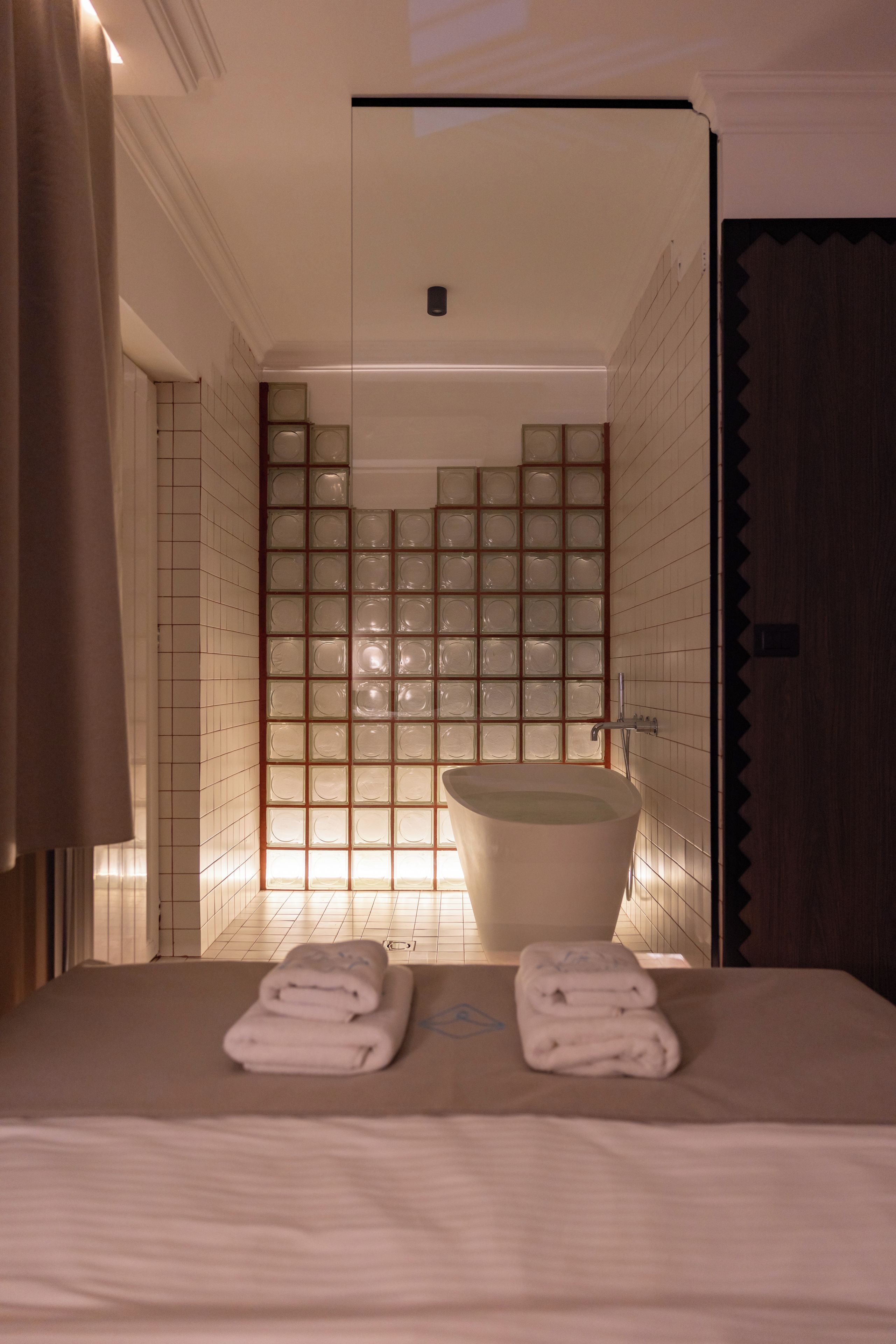 A hotel bathroom with a bathtub, a shower area, and a bed with towels.