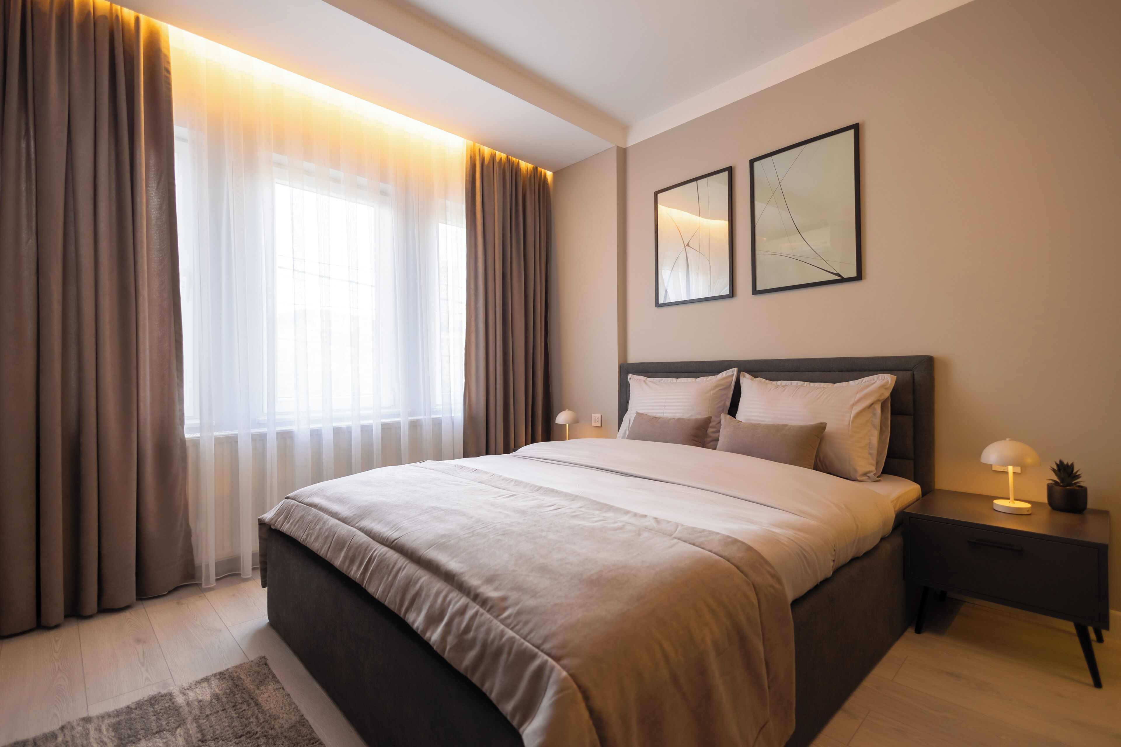 A modern bedroom with a large bed, a nightstand with a lamp, and a window with curtains.