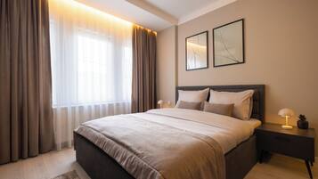 A modern bedroom with a large bed, a nightstand with a lamp, and a window with curtains.