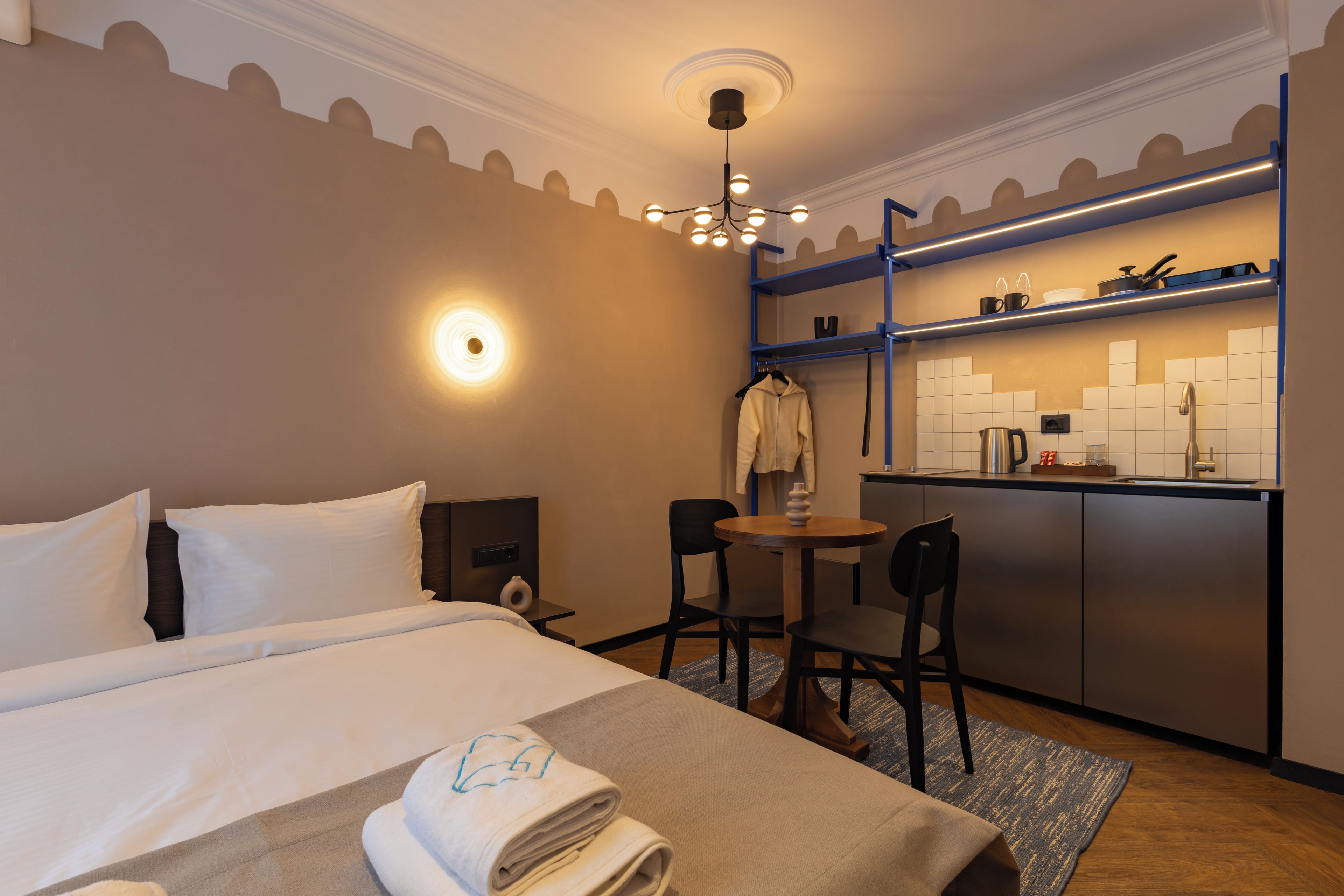 Hotelkamer met een bed, een bureau, een stoel, een kleine tafel, een hanglamp en een kitchenette.
