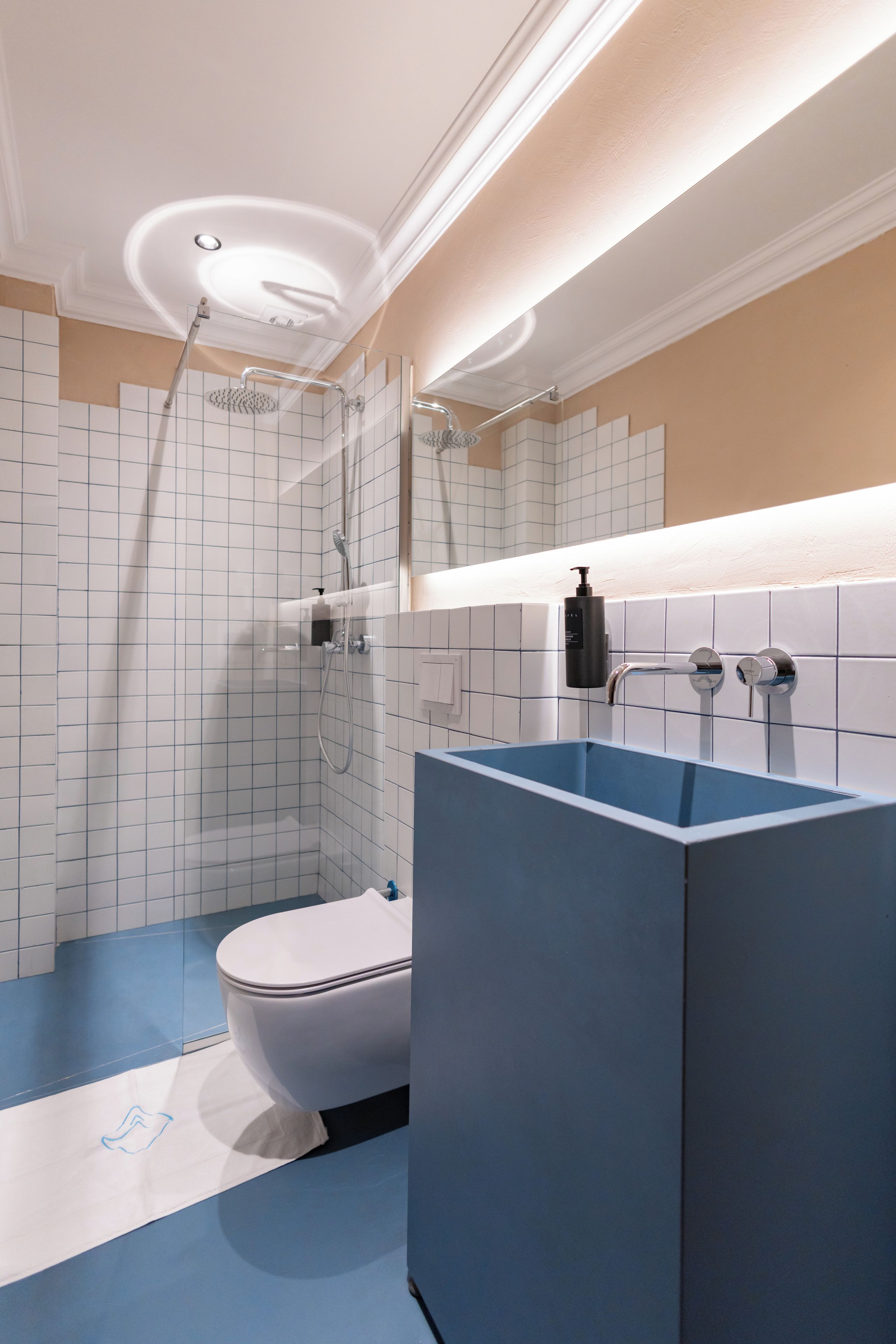 Un bany modern amb un vàter blanc, un lavabo blau i una dutxa amb envàs de vidre.