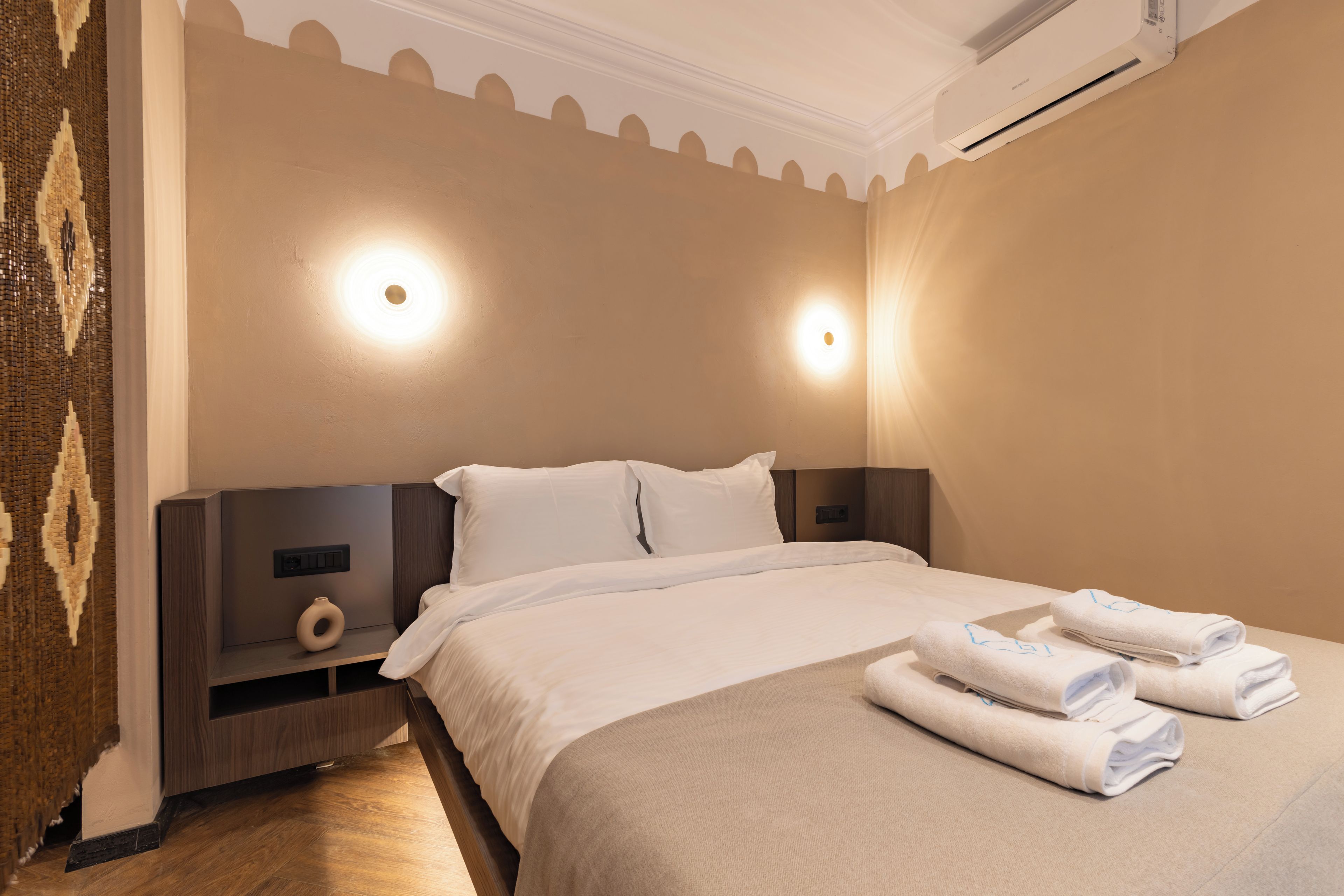 Una habitación de hotel con una cama, mesitas de noche e iluminación en la pared.