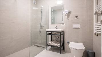 Ein modernes Badezimmer mit Duschkabine aus Glas, Waschbecken mit Handtuchhalter, Toilette und einer kleinen Topfpflanze.