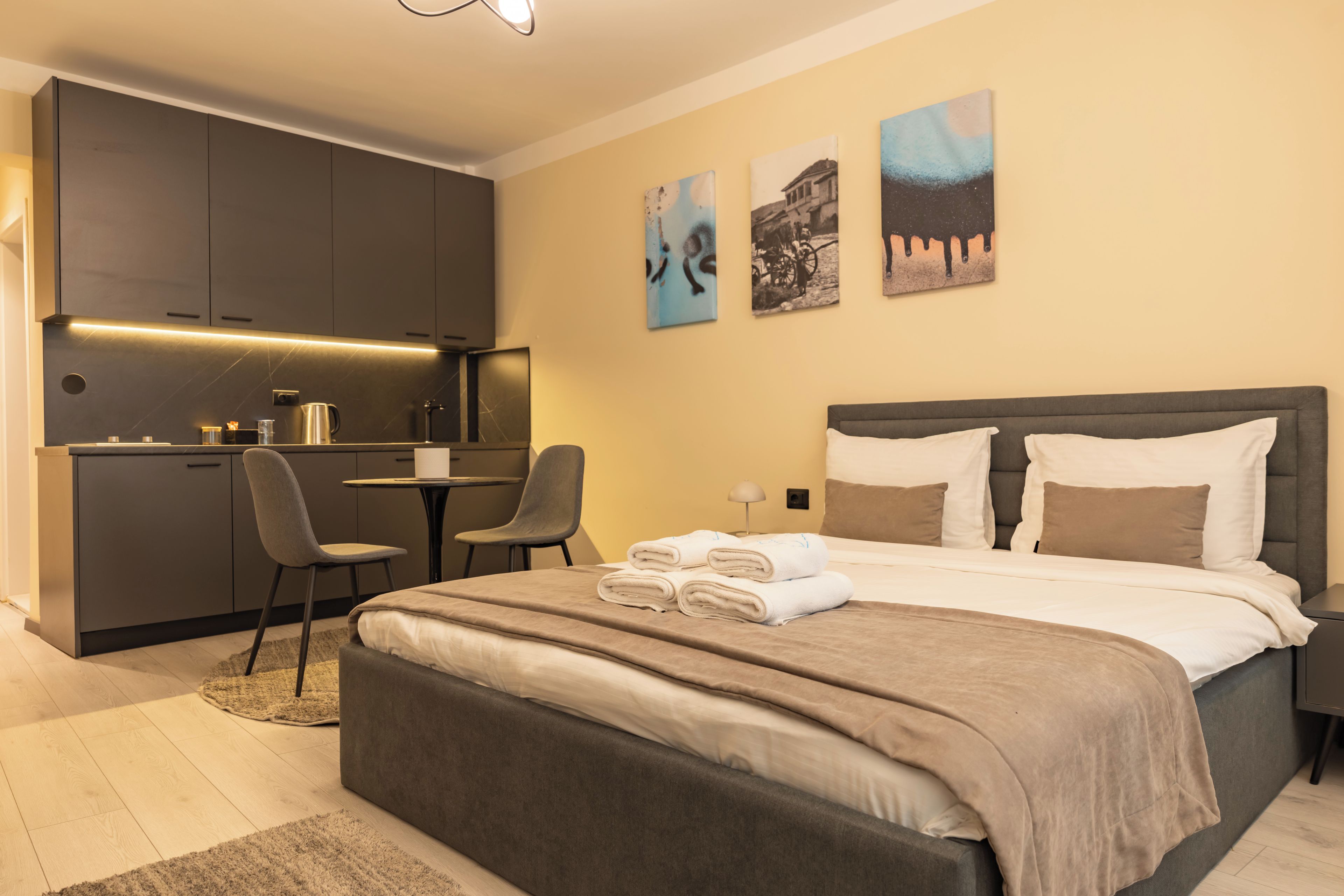 A modern hotel room with a bed, a desk, and a kitchenette.