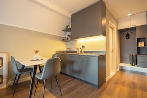 A compact kitchen with a dining area, featuring a modern design with grey cabinetry and a wooden floor. - Prishtina City Apartments (Pristina)