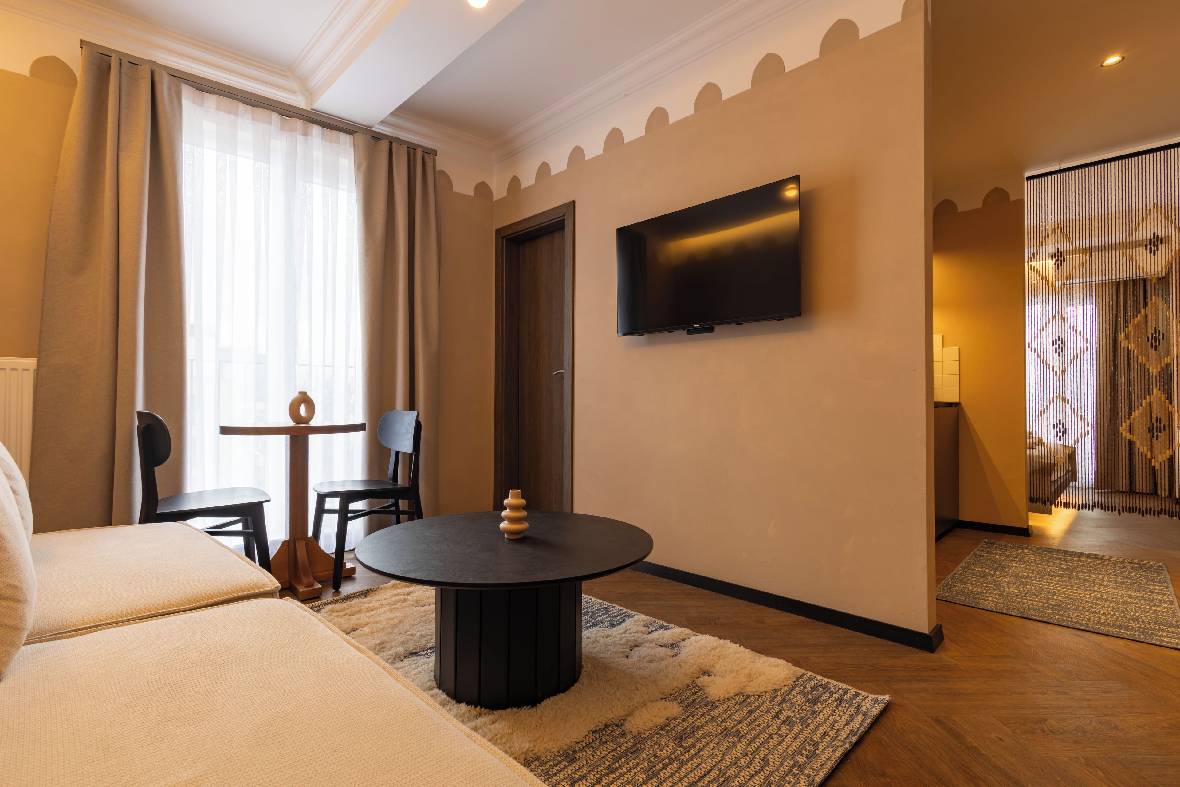 Ein Hotelzimmer mit einem Bett, einem runden Tisch mit Stühlen, einem an der Wand befestigten Fernseher und einer Tür zu einem weiteren Zimmer.