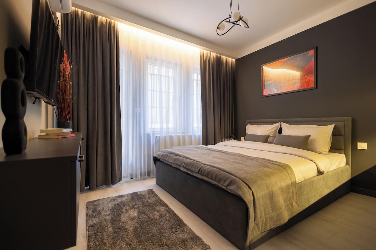 A modern bedroom with a large bed, a desk, a chair, and a window with curtains.