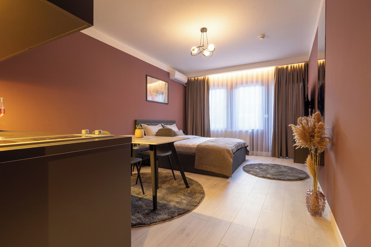 A modern hotel room with a bed, a desk, and a dining area.