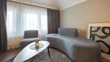 Een moderne woonkamer met een grijze bank, een klein bijzettafeltje en een groot raam met dunne gordijnen.