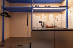 Una cocina compacta con un lavamanos, una tetera y una estantería con utensilios de cocina.