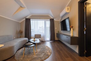 Un salon moderne avec un canapé, une table basse, un téléviseur fixé au mur et une grande fenêtre avec des rideaux.